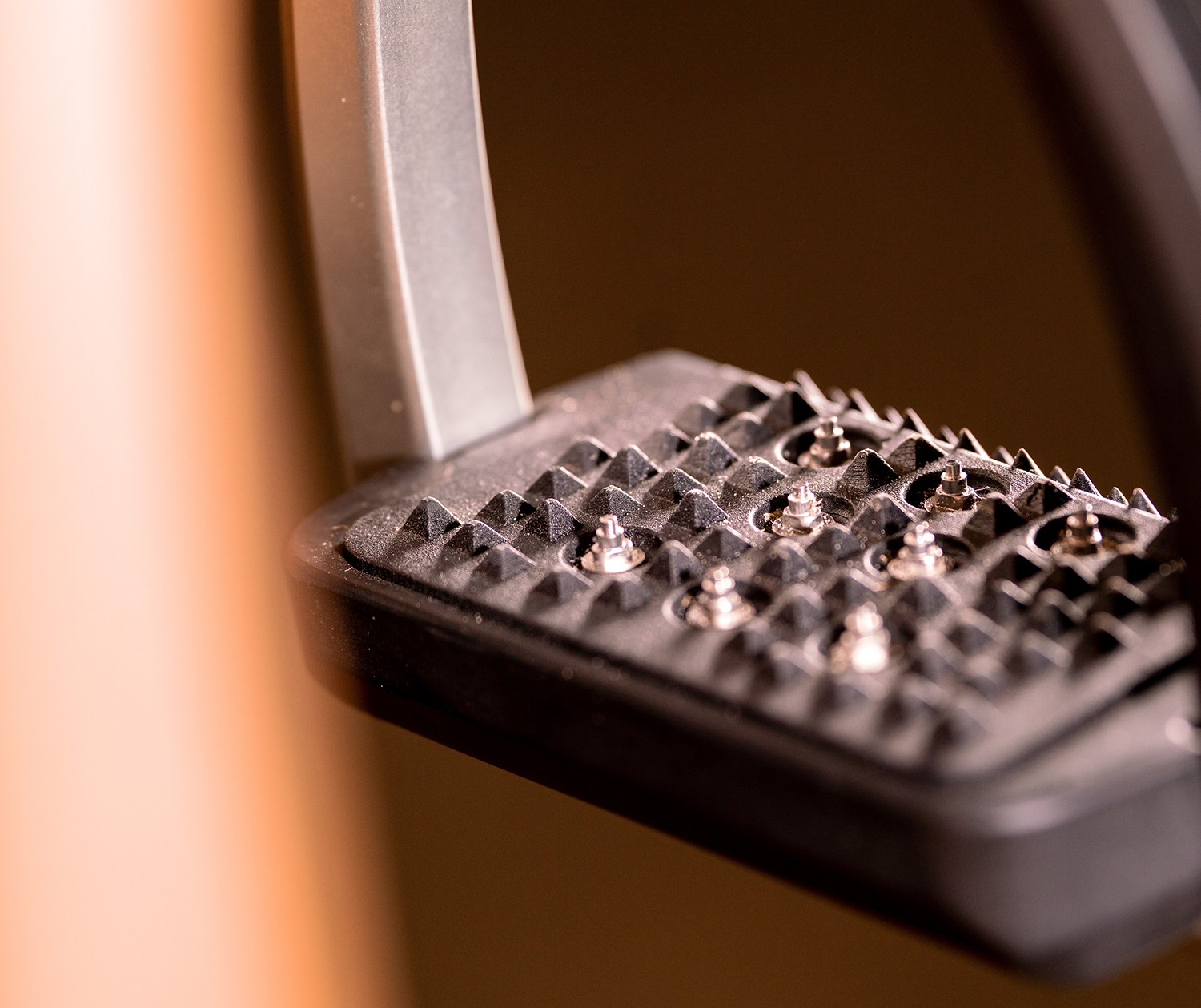 Detailaufnahme eines Fahrradpedals mit rutschfester Oberfläche. Die Oberfläche ist mit kleinen, spitzen Erhebungen versehen, die für besseren Halt sorgen. In der Bildmitte ist die pedalkörperliche Verbindung zu sehen, die aus silbernem Metall besteht. Der Hintergrund ist unscharf und lässt den Fokus auf das Pedal und seine Struktur.