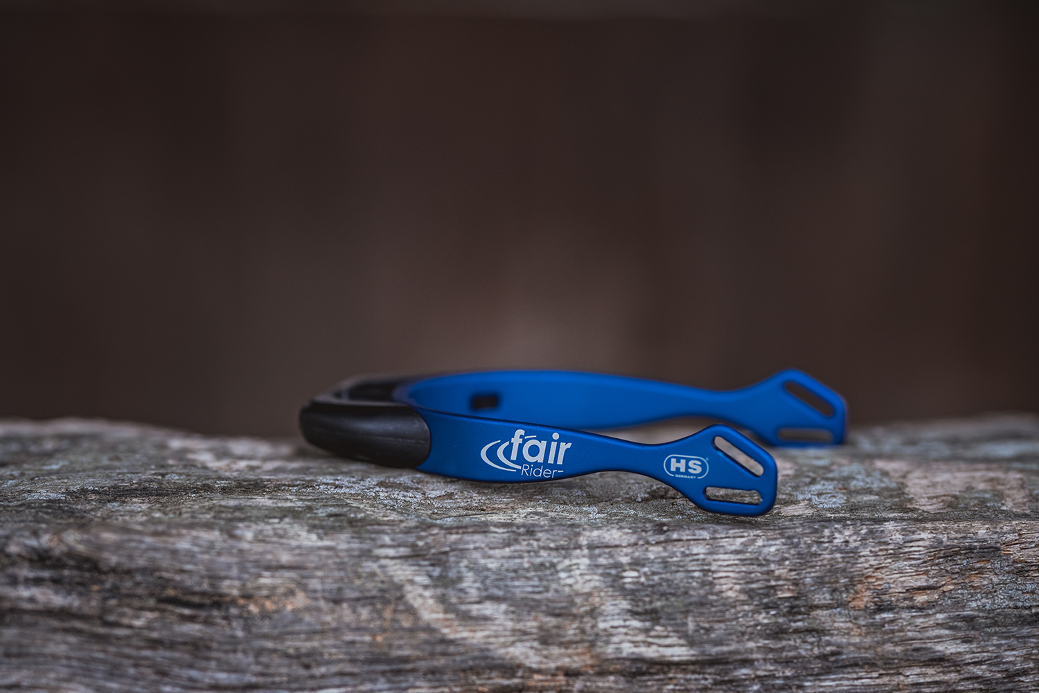 Ein blauer Reifenheber mit dem Aufdruck „fair rider“ liegt auf einem rustikalen Holzbrett. Der Reifenheber hat an einem Ende eine schmale, gebogene Kante, die zum Entfernen von Reifen verwendet wird, und an dem anderen Ende zwei griffähnliche Aussparungen zum besseren Halt. Die Holzoberfläche zeigt eine natürliche Maserung und eine verwitterte Struktur.